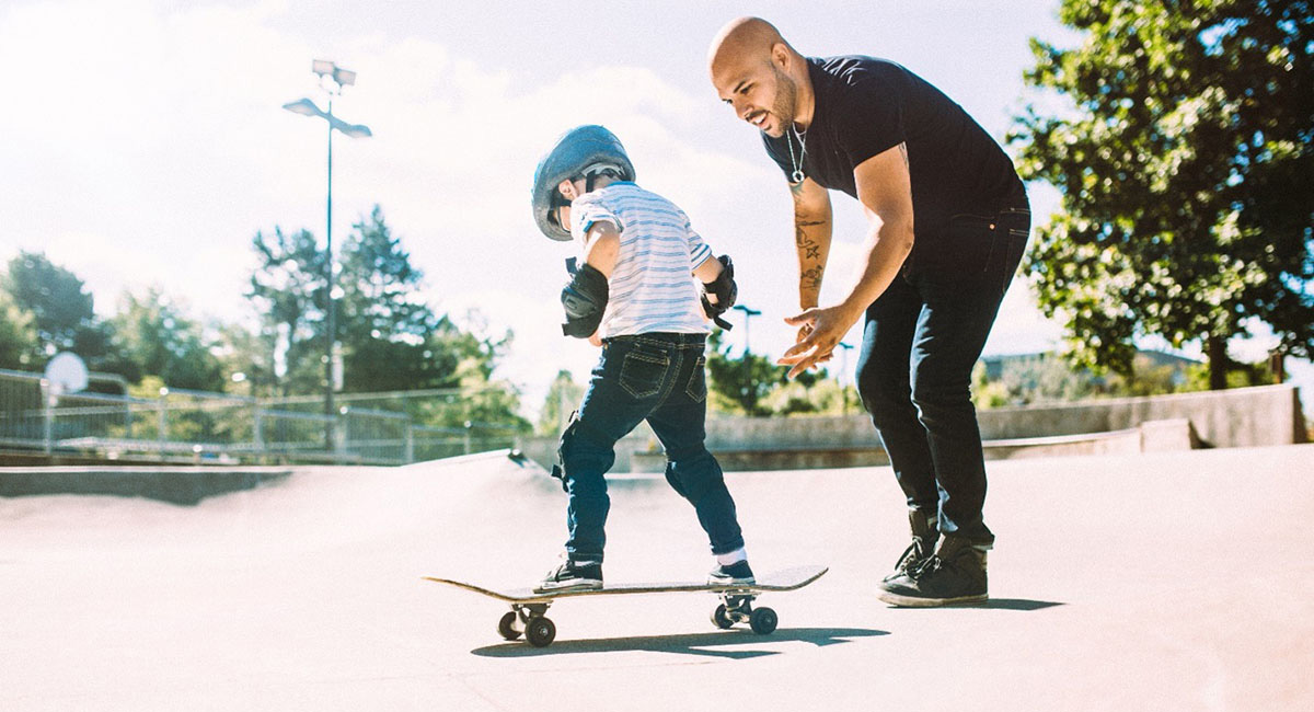 Father showing son how to skateboard at skate park